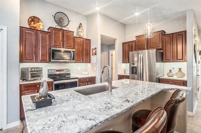 kitchen featuring a kitchen island with sink, sink, stainless steel appliances, and hanging light fixtures