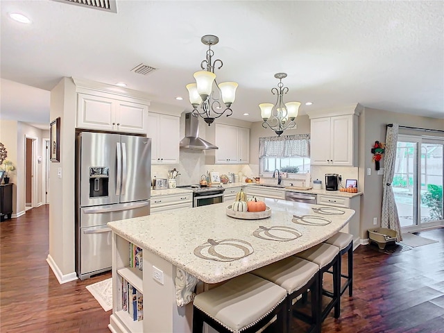 kitchen with decorative light fixtures, white cabinets, a center island, stainless steel appliances, and wall chimney exhaust hood