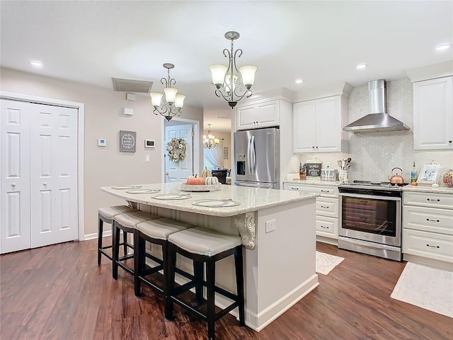 kitchen with wall chimney range hood, white cabinetry, an inviting chandelier, stainless steel appliances, and a kitchen island