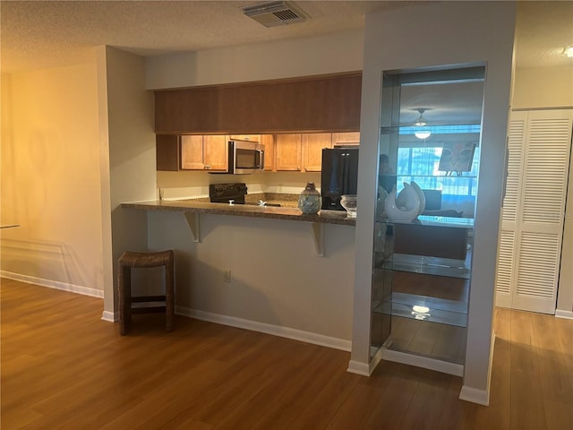 kitchen with a breakfast bar, black appliances, kitchen peninsula, dark wood-type flooring, and a textured ceiling