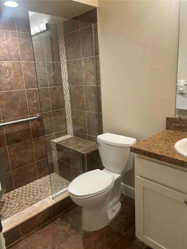 bathroom featuring vanity, tile patterned floors, toilet, and tiled shower