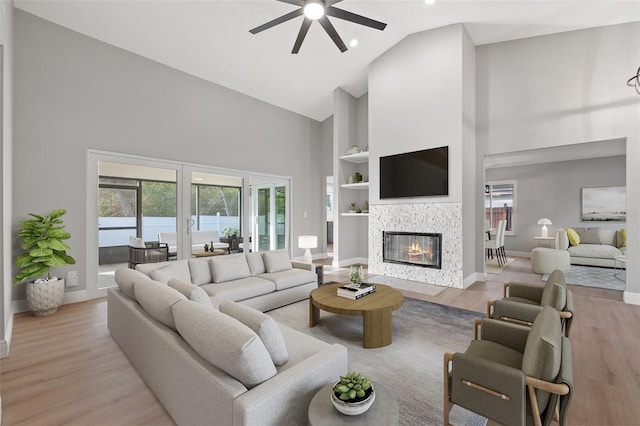 living room with light hardwood / wood-style flooring, a tile fireplace, ceiling fan, high vaulted ceiling, and built in shelves