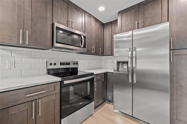 kitchen featuring stainless steel appliances, tasteful backsplash, dark brown cabinetry, light stone countertops, and light hardwood / wood-style floors