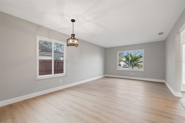 unfurnished room with plenty of natural light, light hardwood / wood-style floors, a chandelier, and a textured ceiling