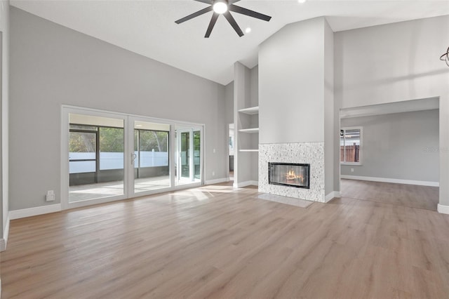 unfurnished living room with built in features, ceiling fan, high vaulted ceiling, a tiled fireplace, and light wood-type flooring