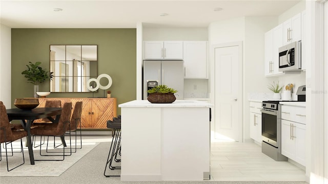 kitchen with a kitchen island, white cabinetry, appliances with stainless steel finishes, and light hardwood / wood-style flooring