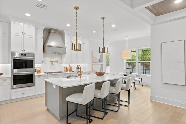 kitchen featuring a breakfast bar area, a kitchen island with sink, white cabinetry, stainless steel appliances, and custom exhaust hood