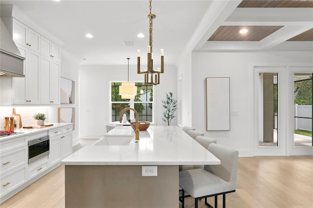 kitchen featuring hanging light fixtures, a kitchen island with sink, wall chimney range hood, and a kitchen bar