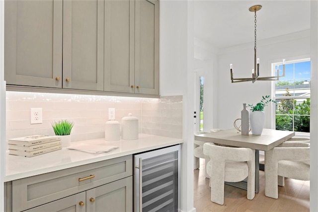 kitchen with gray cabinetry, beverage cooler, backsplash, hanging light fixtures, and light wood-type flooring