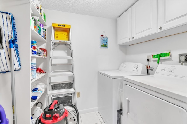 clothes washing area with light tile patterned flooring, cabinets, washer and dryer, and a textured ceiling