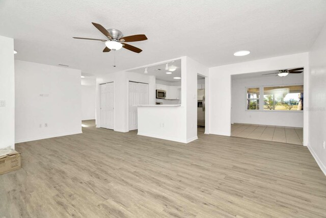 unfurnished living room featuring ceiling fan, a textured ceiling, and light hardwood / wood-style flooring