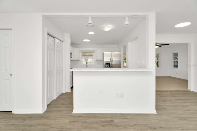 kitchen with stainless steel refrigerator with ice dispenser, white cabinetry, kitchen peninsula, and light hardwood / wood-style floors