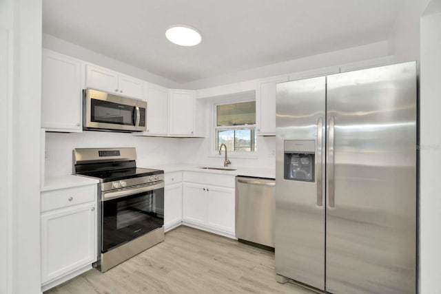 kitchen with stainless steel appliances, white cabinetry, sink, and light hardwood / wood-style flooring