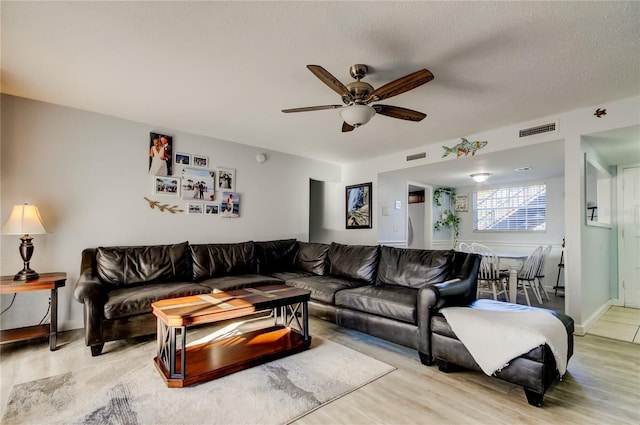 living room featuring ceiling fan, a textured ceiling, and light wood-type flooring