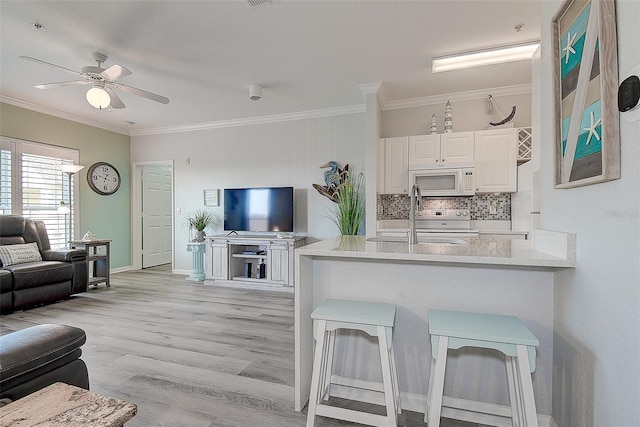 kitchen with sink, white appliances, a breakfast bar area, white cabinetry, and kitchen peninsula