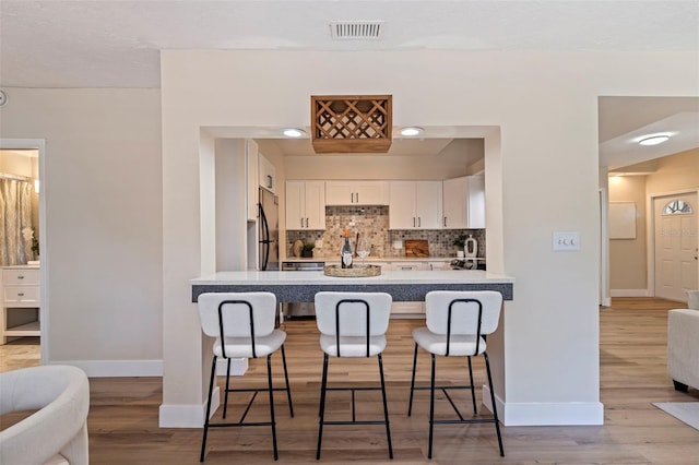 kitchen with a kitchen bar, light hardwood / wood-style flooring, stainless steel fridge, white cabinets, and tasteful backsplash