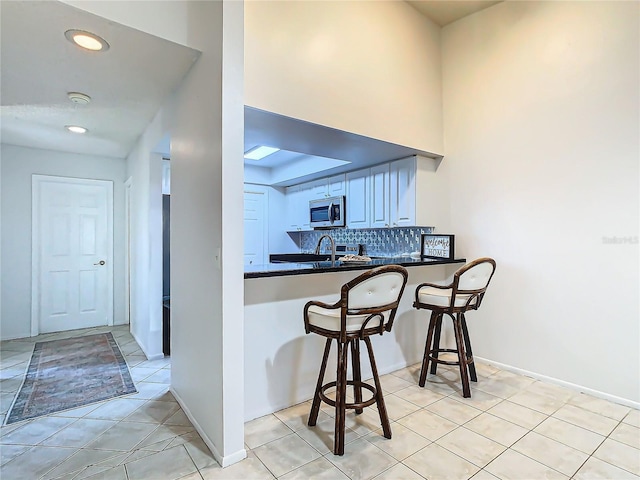 kitchen featuring tasteful backsplash, kitchen peninsula, sink, and light tile patterned floors