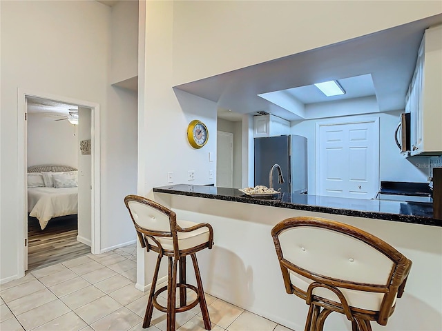 kitchen featuring light tile patterned floors, range, dark stone countertops, refrigerator, and kitchen peninsula