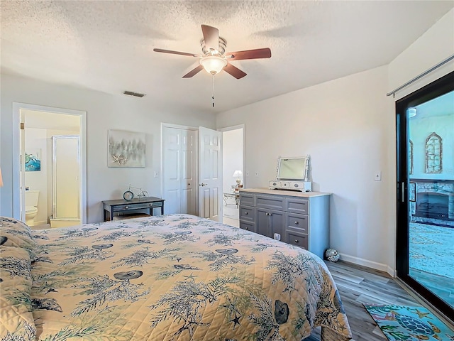 bedroom with ceiling fan, ensuite bath, light hardwood / wood-style flooring, and a textured ceiling