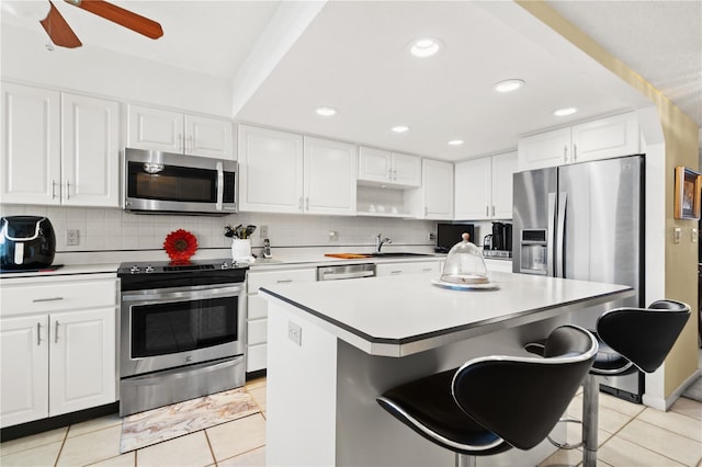 kitchen with a kitchen island, backsplash, white cabinets, a kitchen breakfast bar, and stainless steel appliances