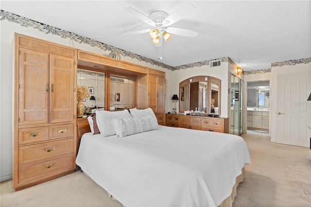 bedroom with ceiling fan, ensuite bathroom, light carpet, and a textured ceiling