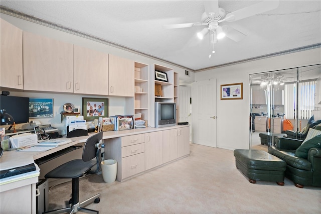 office space with crown molding, built in desk, light carpet, a textured ceiling, and ceiling fan