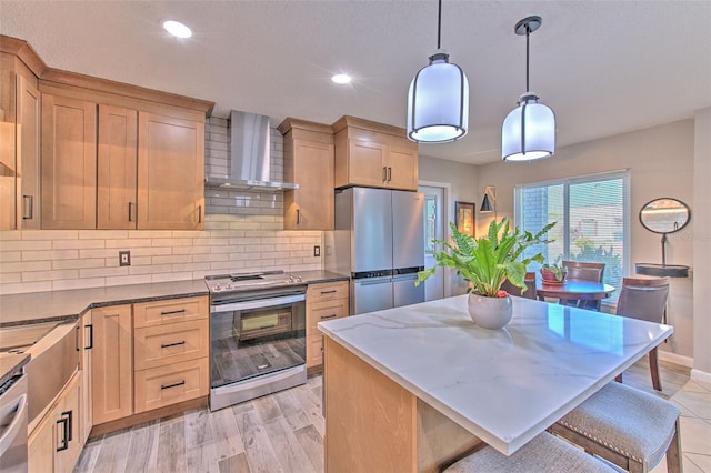 kitchen with pendant lighting, stainless steel appliances, light wood-style flooring, decorative backsplash, and wall chimney range hood