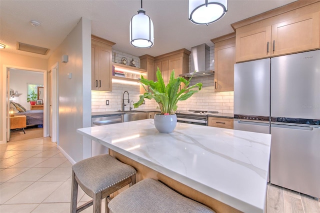 kitchen with light tile patterned flooring, a sink, appliances with stainless steel finishes, light stone countertops, and wall chimney exhaust hood