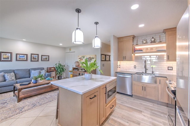 kitchen featuring open floor plan, light brown cabinetry, appliances with stainless steel finishes, and a sink