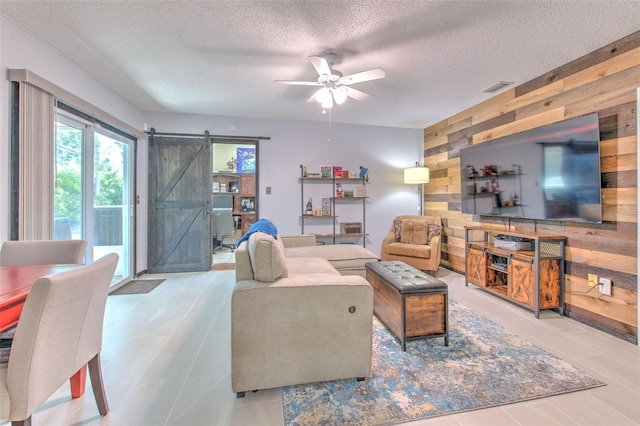 living area with a barn door, wooden walls, visible vents, and a textured ceiling