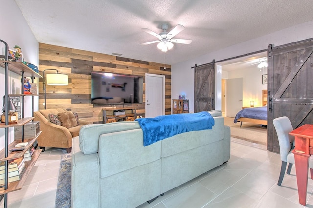 tiled living room featuring a barn door, an accent wall, a ceiling fan, wooden walls, and a textured ceiling