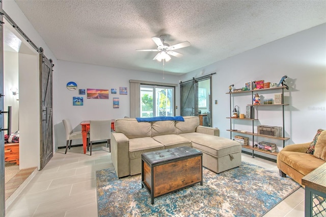 living area with ceiling fan, a barn door, a textured ceiling, and light tile patterned floors