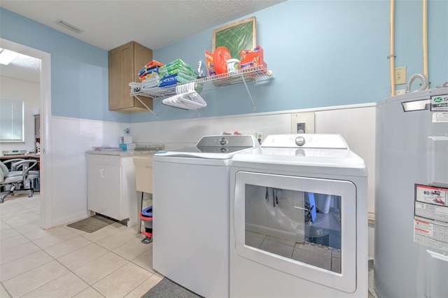 washroom with light tile patterned flooring, separate washer and dryer, visible vents, water heater, and cabinet space