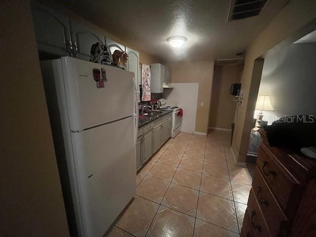 kitchen with white appliances, light tile patterned floors, baseboards, visible vents, and a textured ceiling