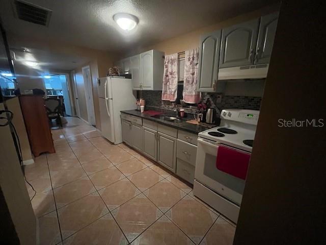 kitchen with light tile patterned floors, under cabinet range hood, white appliances, visible vents, and dark countertops