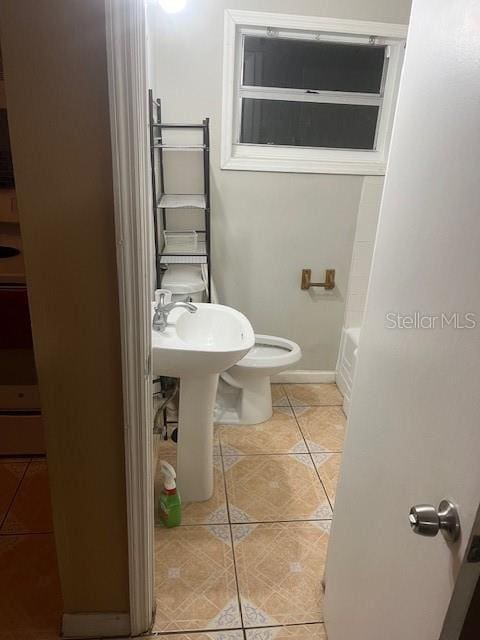 full bath featuring toilet, a tub to relax in, baseboards, and tile patterned floors