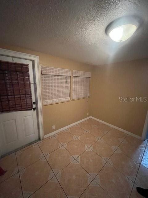 unfurnished room with light tile patterned floors, baseboards, and a textured ceiling