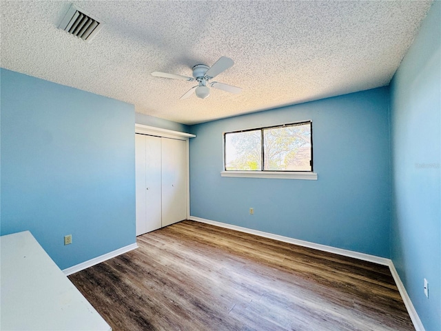 unfurnished bedroom with a closet, wood finished floors, visible vents, and baseboards