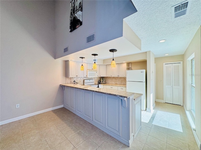 kitchen with white appliances, visible vents, light stone counters, a peninsula, and hanging light fixtures