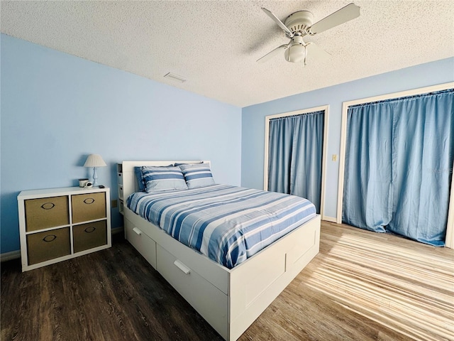 bedroom featuring a textured ceiling, dark wood-type flooring, visible vents, and a ceiling fan