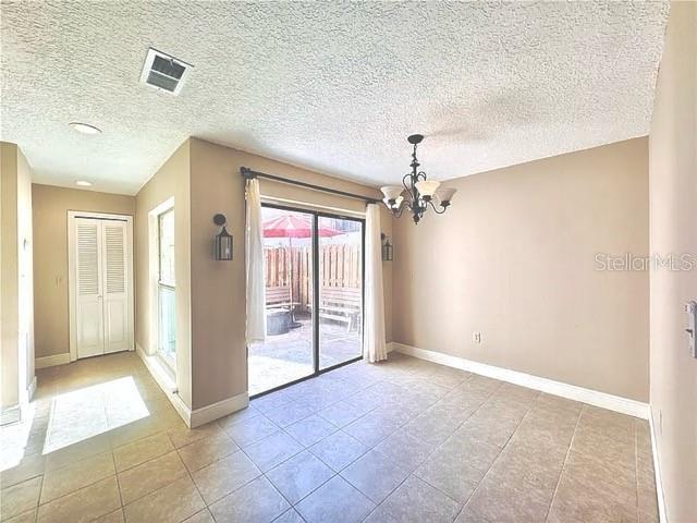 unfurnished room featuring visible vents, a textured ceiling, baseboards, and an inviting chandelier