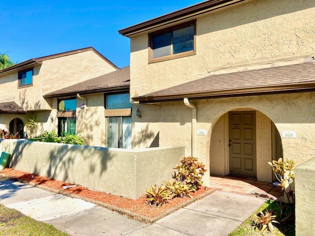 entrance to property with a shingled roof, fence, and stucco siding