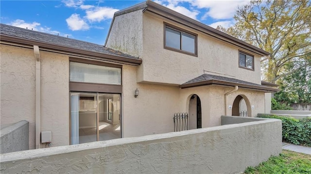 exterior space featuring a fenced front yard, roof with shingles, and stucco siding