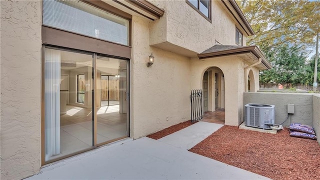 view of exterior entry featuring central air condition unit, a shingled roof, and stucco siding