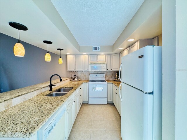 kitchen with a peninsula, white appliances, a sink, white cabinetry, and hanging light fixtures