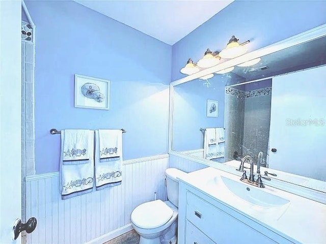 bathroom with toilet, vanity, a shower, and wainscoting