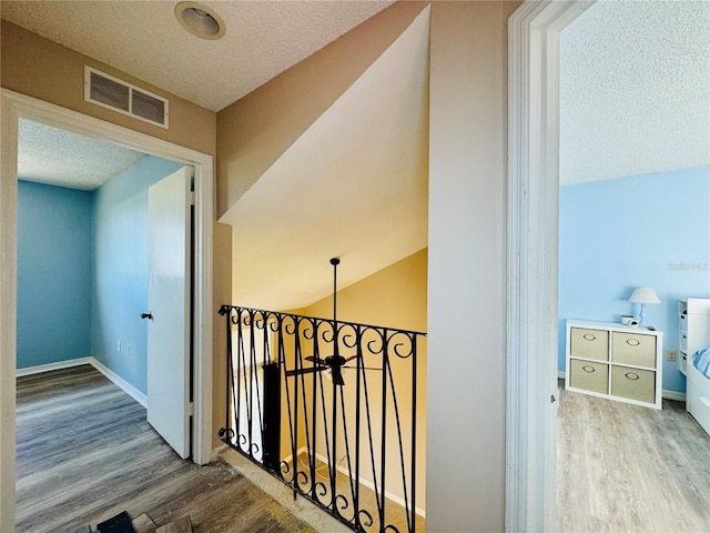 hallway with baseboards, a textured ceiling, visible vents, and wood finished floors