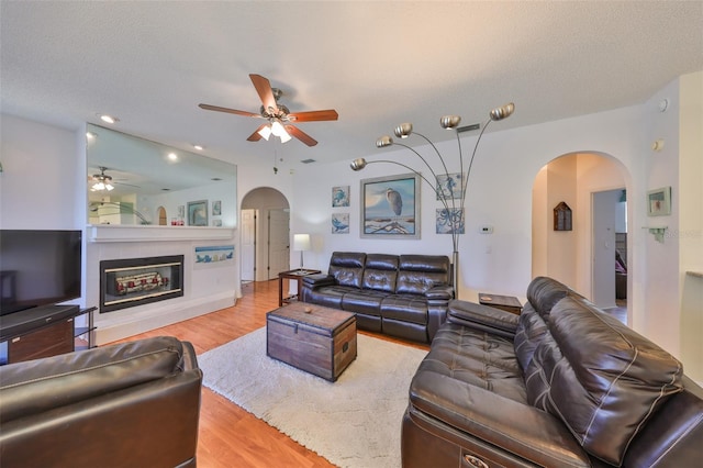 living room featuring a tiled fireplace, ceiling fan, light hardwood / wood-style flooring, and a textured ceiling