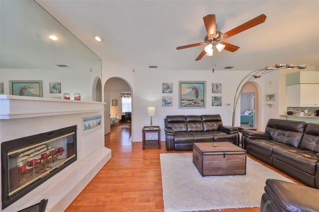 living room with a tiled fireplace, ceiling fan, light hardwood / wood-style floors, and a textured ceiling