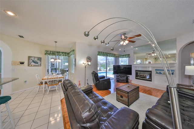 tiled living room featuring ceiling fan with notable chandelier and a textured ceiling